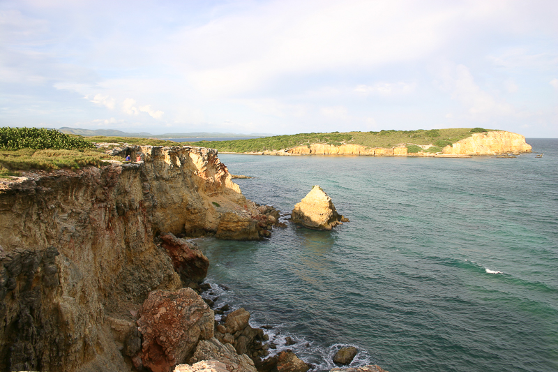Punta Borinquen cove — golden cliffs, a sea stack, and the endless Atlantic beyond